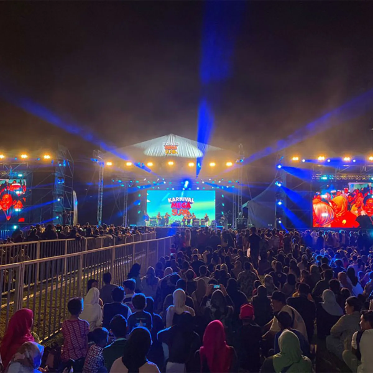 Large outdoor audience watching a brightly lit stage at night
