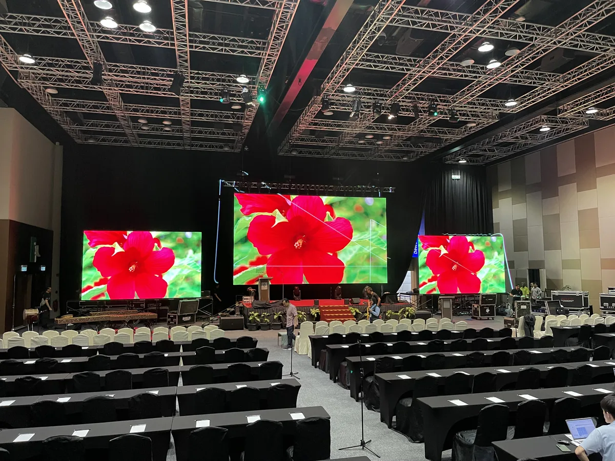 Three LED screens under truss above rows of conference seating