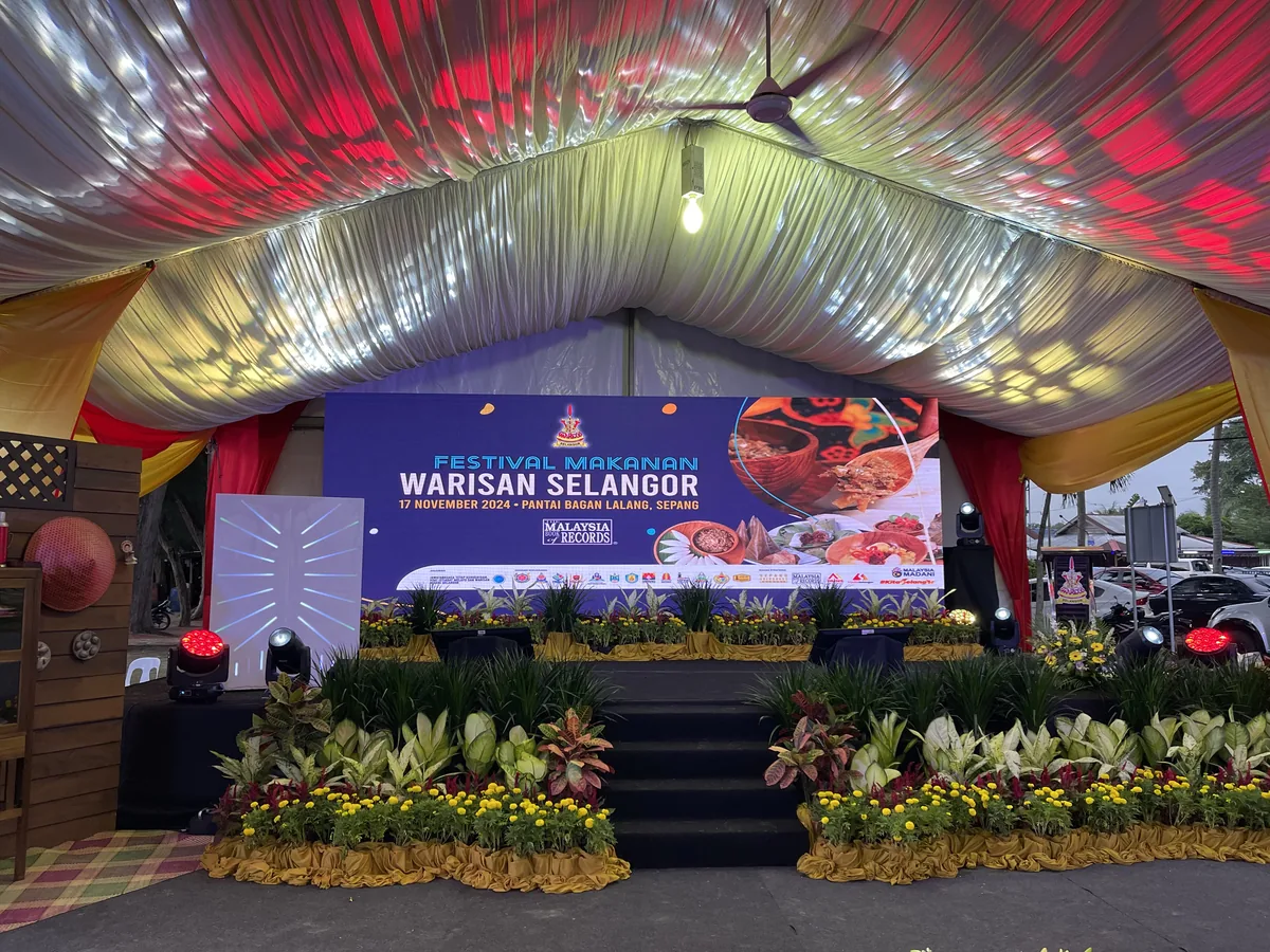 Red-draped marquee stage with flower beds and a festival banner