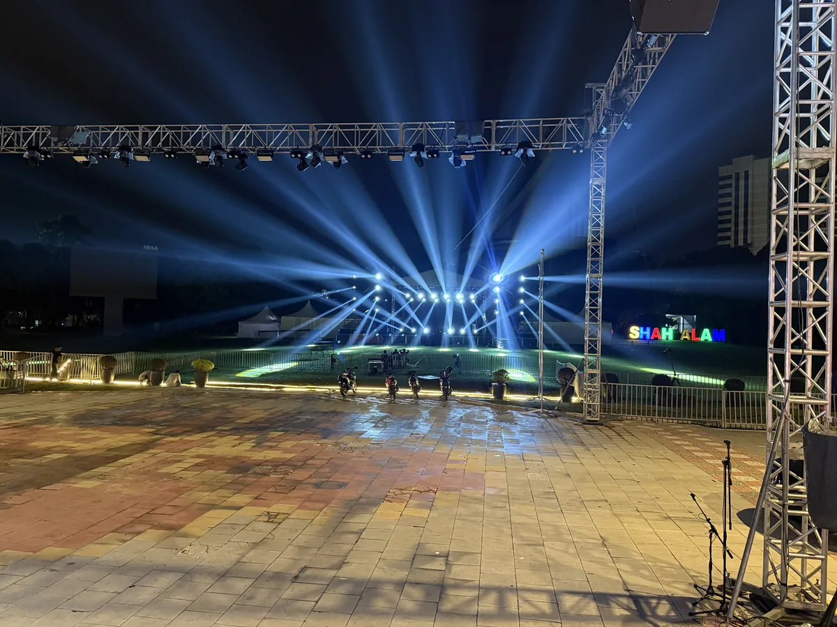 Outdoor truss rig sending blue beams over an open-air stage