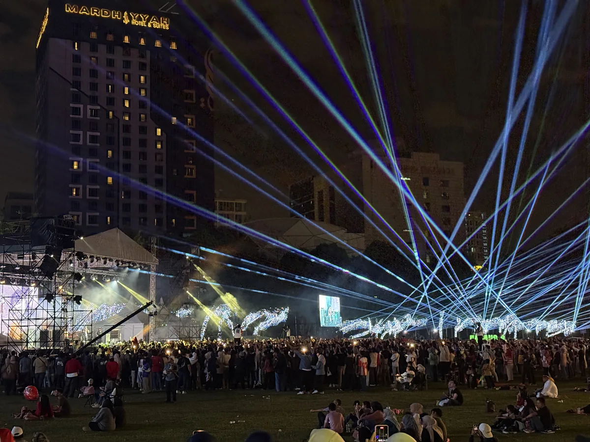 Blue laser beams over a crowd on a lawn beside a lit high-rise